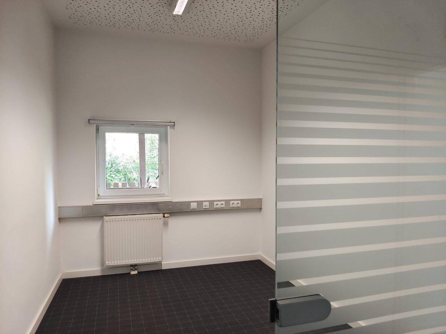 Kleiner Büroraum mit Fenster, Heizkörper und Milchglaswand für Privatsphäre.