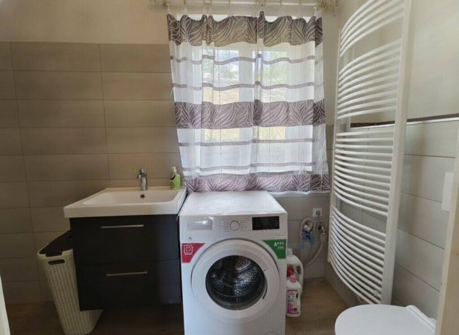 Funktionales Badezimmer mit Waschbecken, Waschmaschine und Handtuchheizkörper.