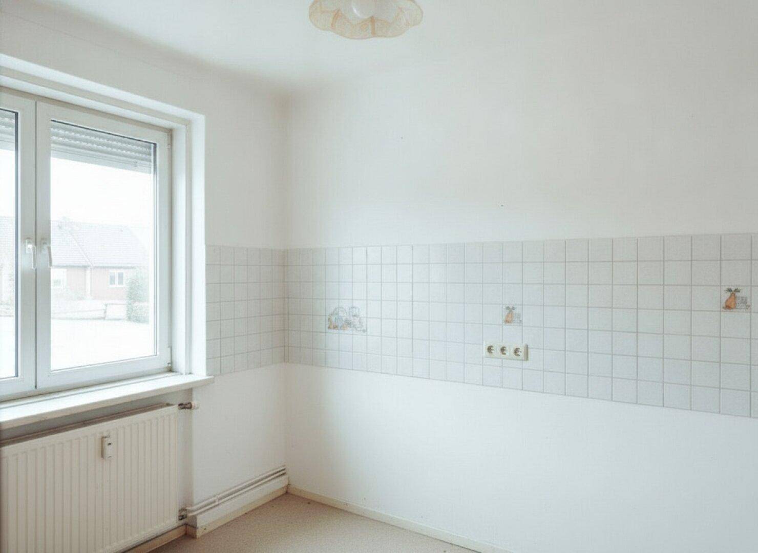 Heller, leerer Küchenraum mit weißen Wandfliesen, Fenster und Heizkörper.
