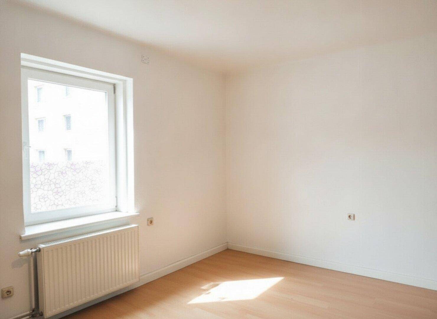 Geräumiger, heller Raum mit Holzfußboden, großem Fenster und Heizkörper.