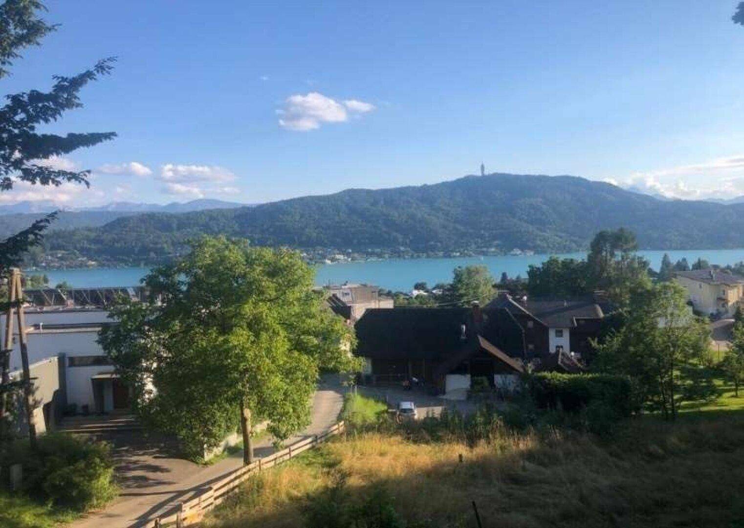 Malerische Landschaft mit einem See, umgeben von grünen Hügeln und Bergen unter blauem Himmel.