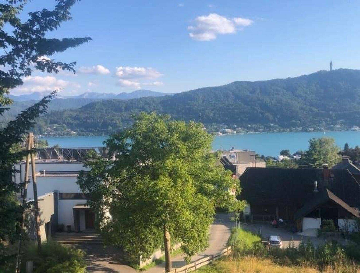 Sonniger Ausblick auf einen blauen See, umrahmt von grünen Bäumen und Bergen.