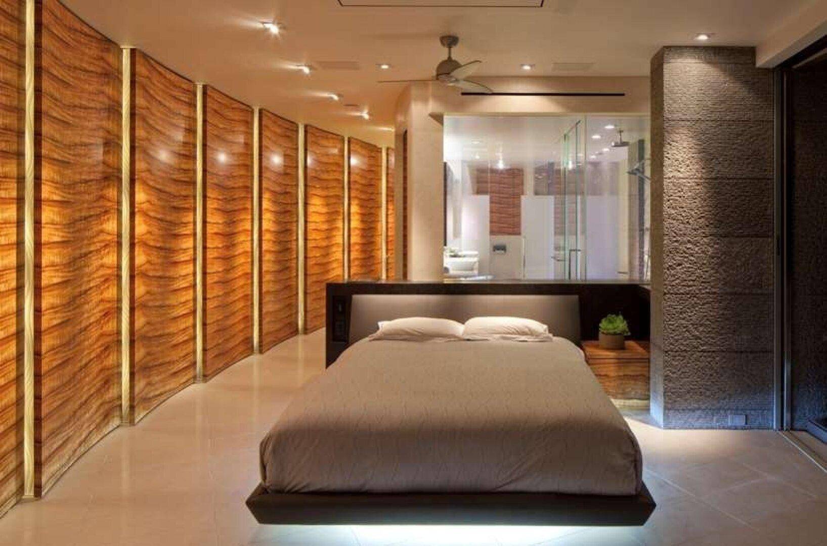 Luxuriöses Schlafzimmer mit indirekter Beleuchtung, Holzwandverkleidung und offenem Badbereich.