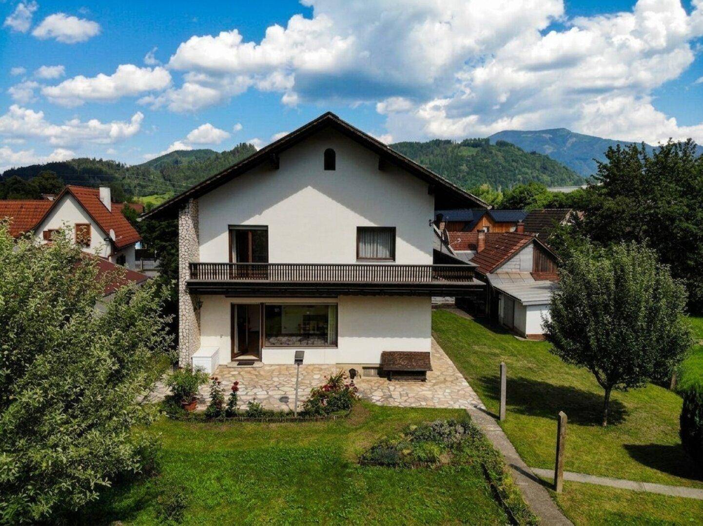 Vorderansicht des Hauses mit Terrasse und Balkon, umgeben von viel Grün.