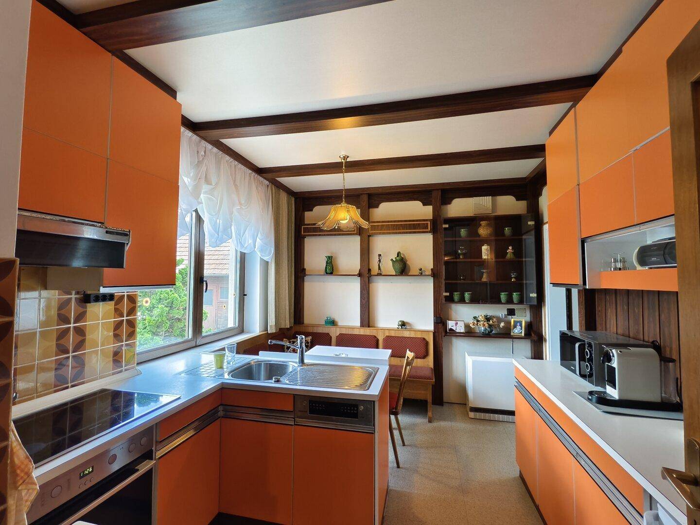 Küche im Retro-Stil mit orangefarbenen Schränken, Holzbalken und Essbereich.