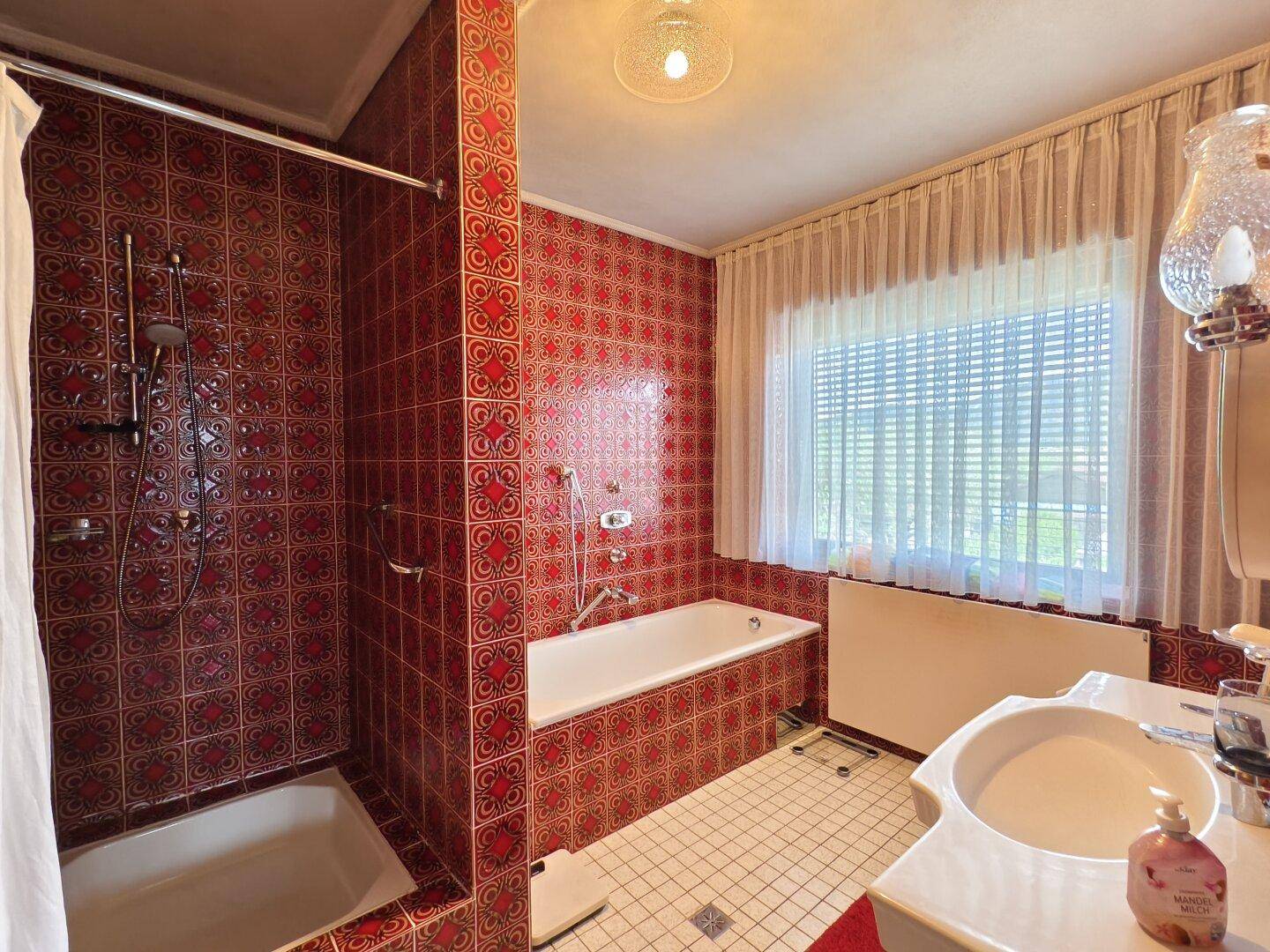 Badezimmer mit roten Fliesen, Badewanne, Dusche und Fenster für Tageslicht.