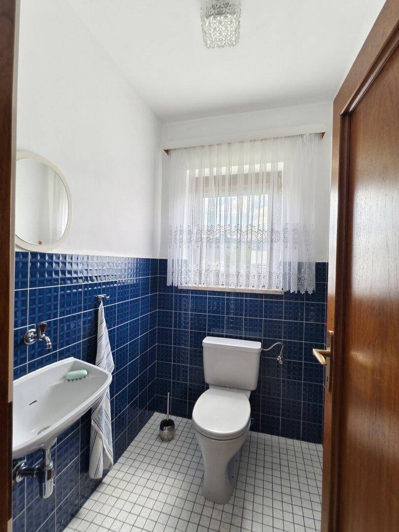 Separate Gästetoilette mit blauen Fliesen, kleinem Waschbecken und Fenster.