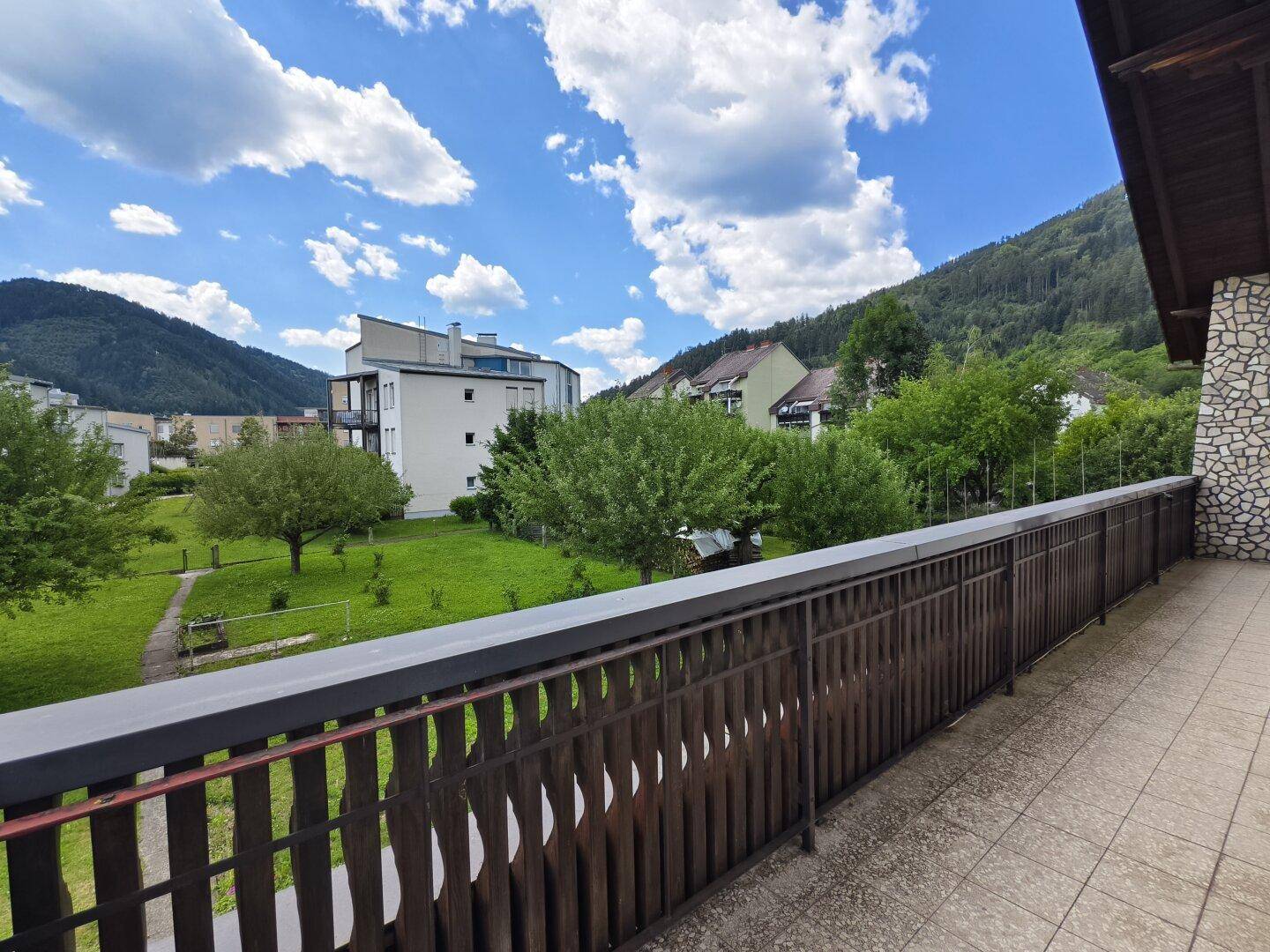 Balkon mit Holzgeländer und weitem Blick über den Garten und die umliegende Landschaft.