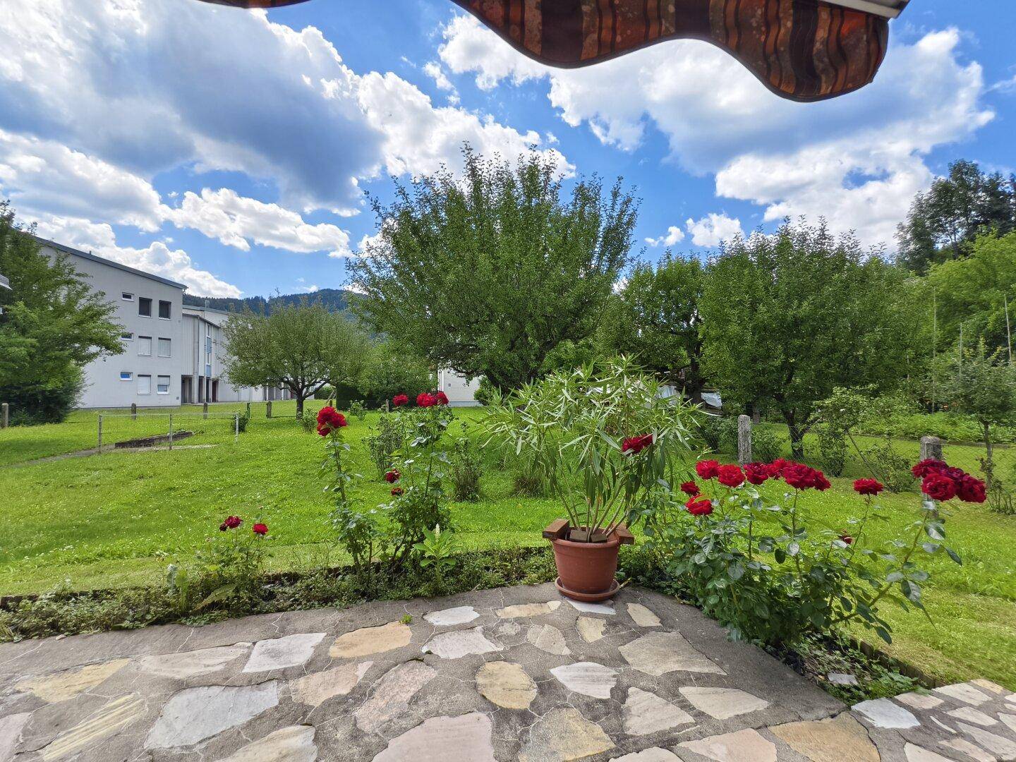 Gemütliche Terrasse mit Rosen und Blick auf den weitläufigen grünen Garten.