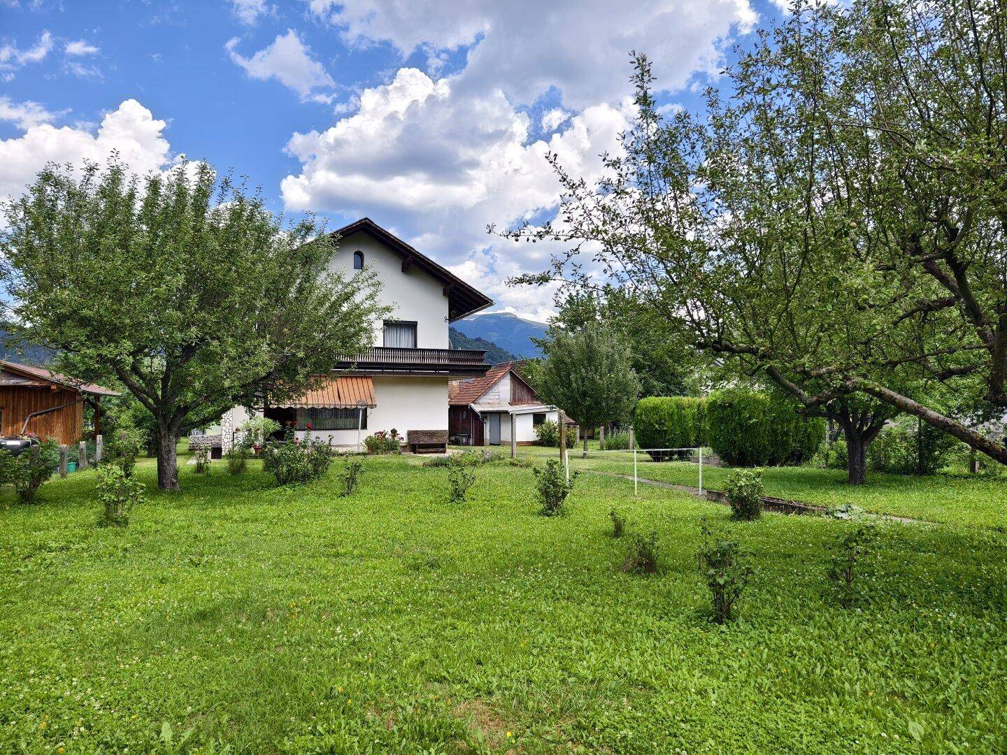Weitläufiger Garten mit Obstbäumen und dem Wohnhaus im Hintergrund unter blauem Himmel.