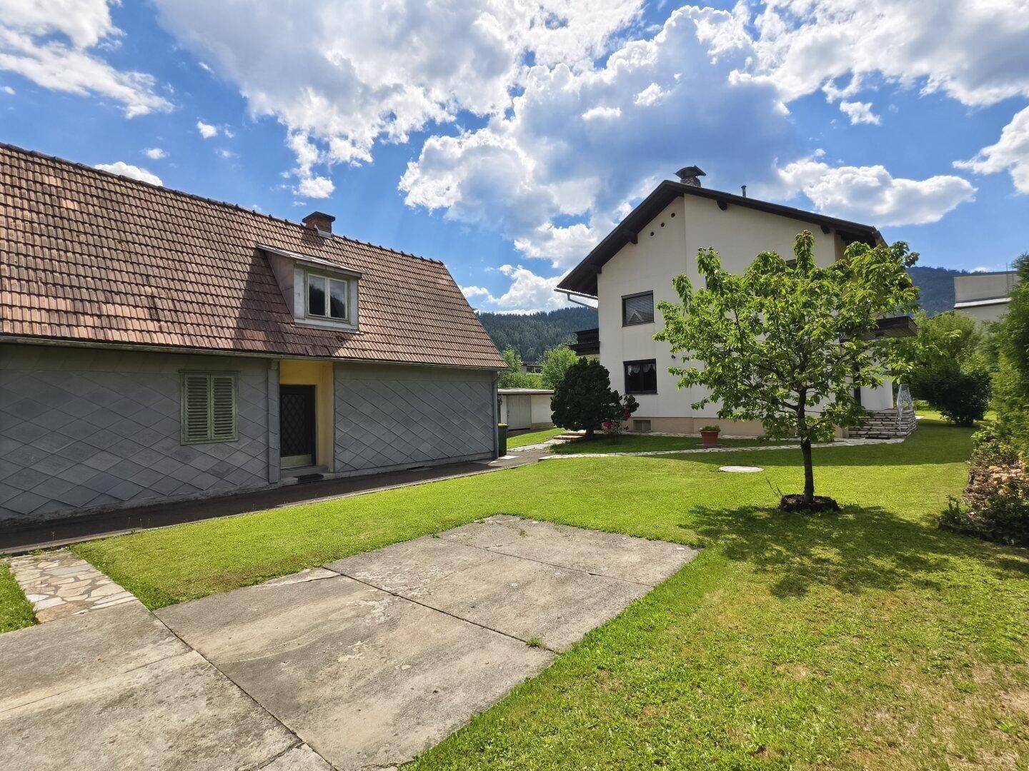 Ansicht des Hauses und eines Nebengebäudes mit Zufahrt und Rasenfläche.