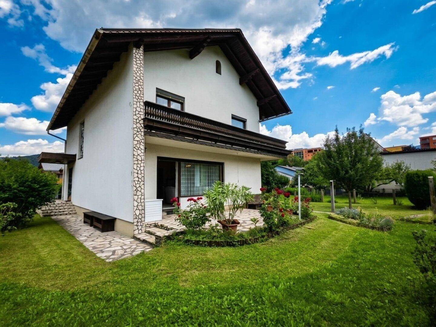 Seitliche Ansicht des Hauses mit einer gepflasterten Terrasse und Blumenbeeten.