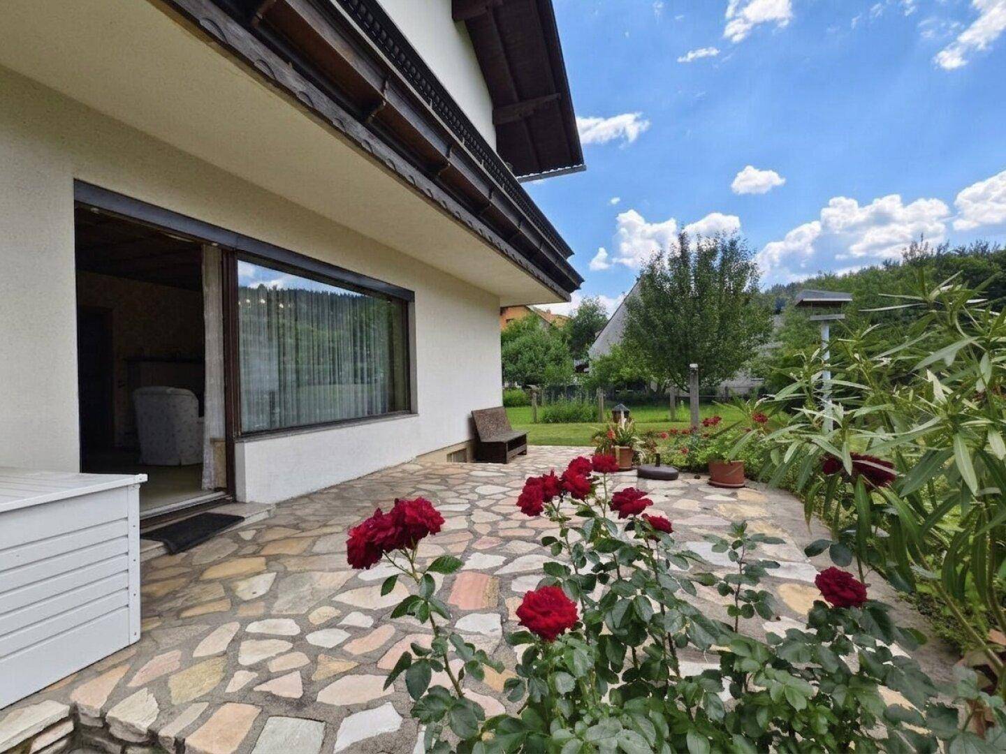 Sonniger Terrassenbereich mit Steinplatten und blühenden Rosen, angrenzend an das Wohnzimmer.