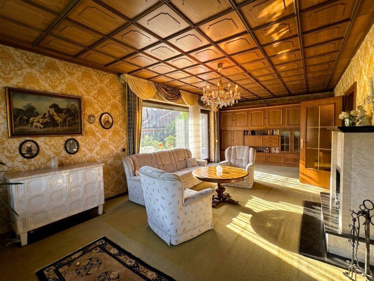 Helles Wohnzimmer mit Holzkassettendecke, Kamin und Blick in den Garten.