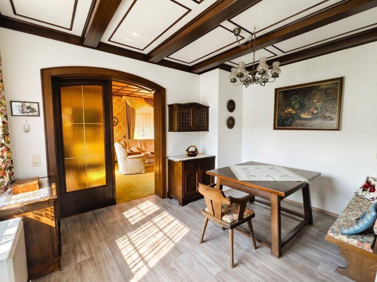 Esszimmer mit Holzbalkendecke, traditionellen Möbeln und Zugang zum Wohnzimmer.