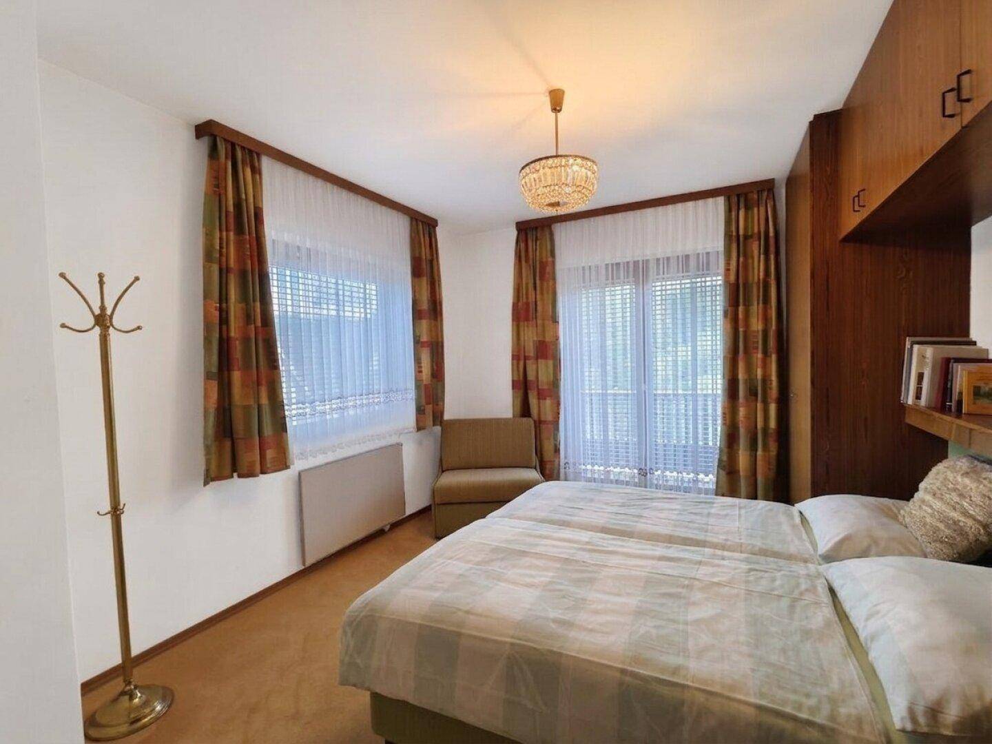 Schlafzimmer mit zwei Einzelbetten, Einbauschränken und Fenstern mit Vorhängen.