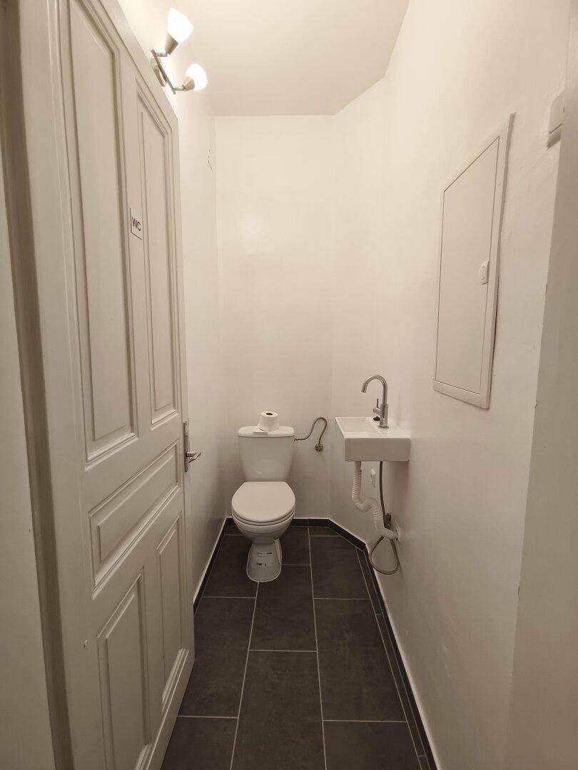 Kleine Gästetoilette mit WC, Waschbecken und dunklen Bodenfliesen in schlichtem Design.