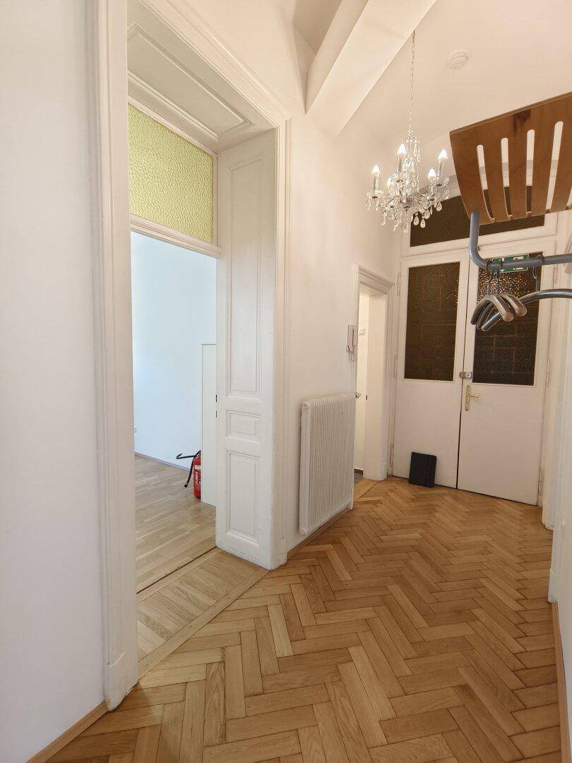 Flur mit Fischgrätparkett, Kronleuchter und einer Garderobe, die zu weiteren Räumen führt.