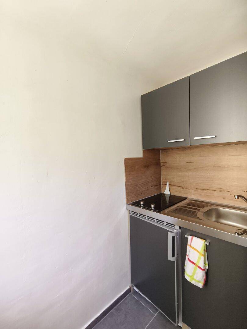 Kleine Küchenzeile mit grauen Schränken, Spüle und Kochfeld, ideal für kompakte Wohnlösungen.