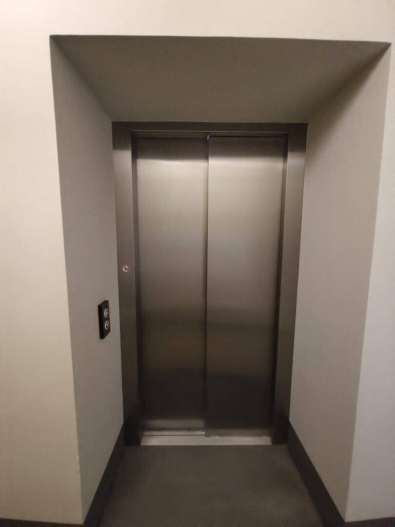 Moderner Aufzug mit Edelstahltüren in einem Flur des Gebäudes.