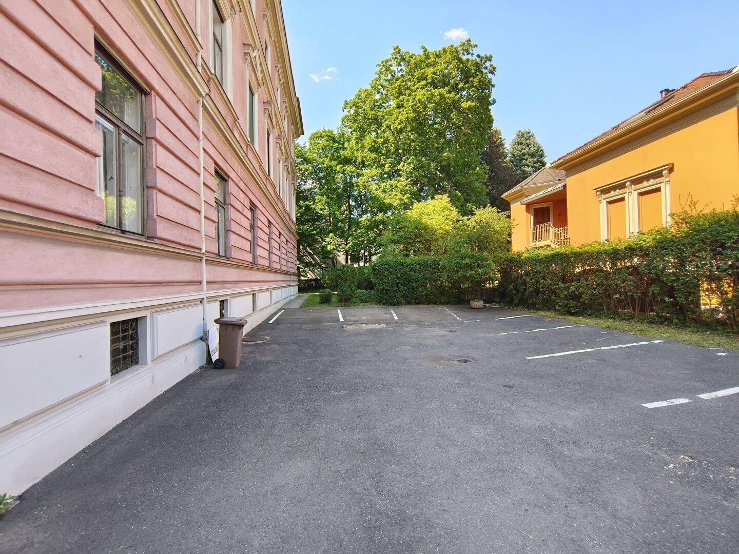 Parkplätze neben dem historischen Gebäude mit Hecke und Bäumen im Hintergrund.