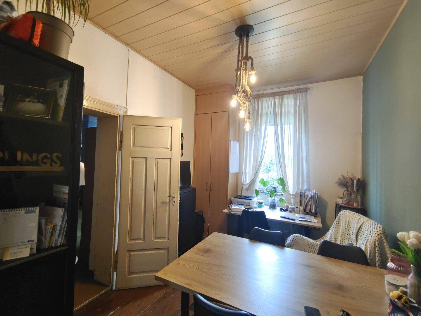 Helles Arbeitszimmer mit Holztisch, Stuhl und einem Fenster, das viel Tageslicht hereinlässt.