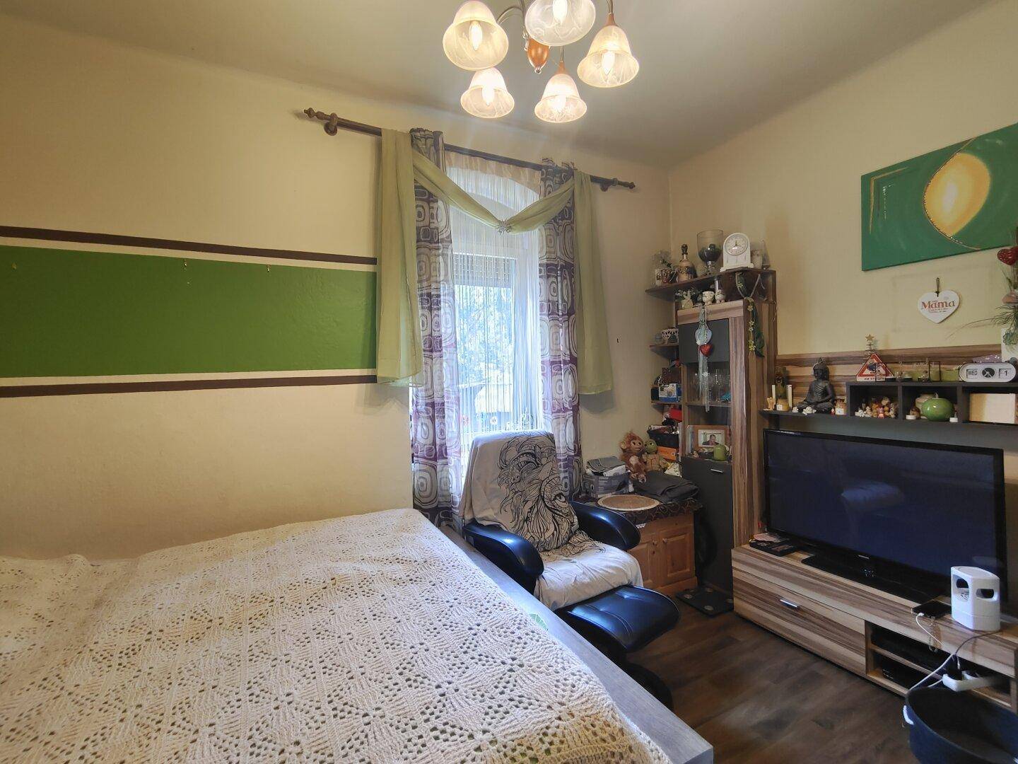 Schlafzimmer mit Bett, Fernseher und grün-weiß gestreiften Wänden, hell und freundlich gestaltet.