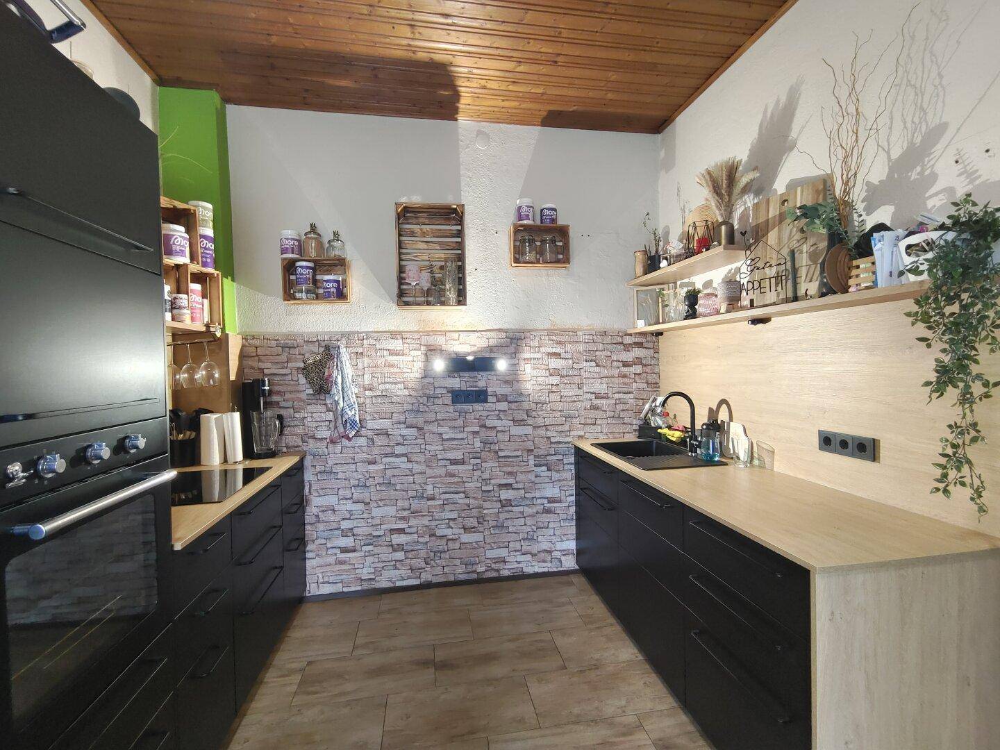 Moderne Küche mit schwarzen Schränken, Holzarbeitsplatten und einer Steinoptik-Rückwand.