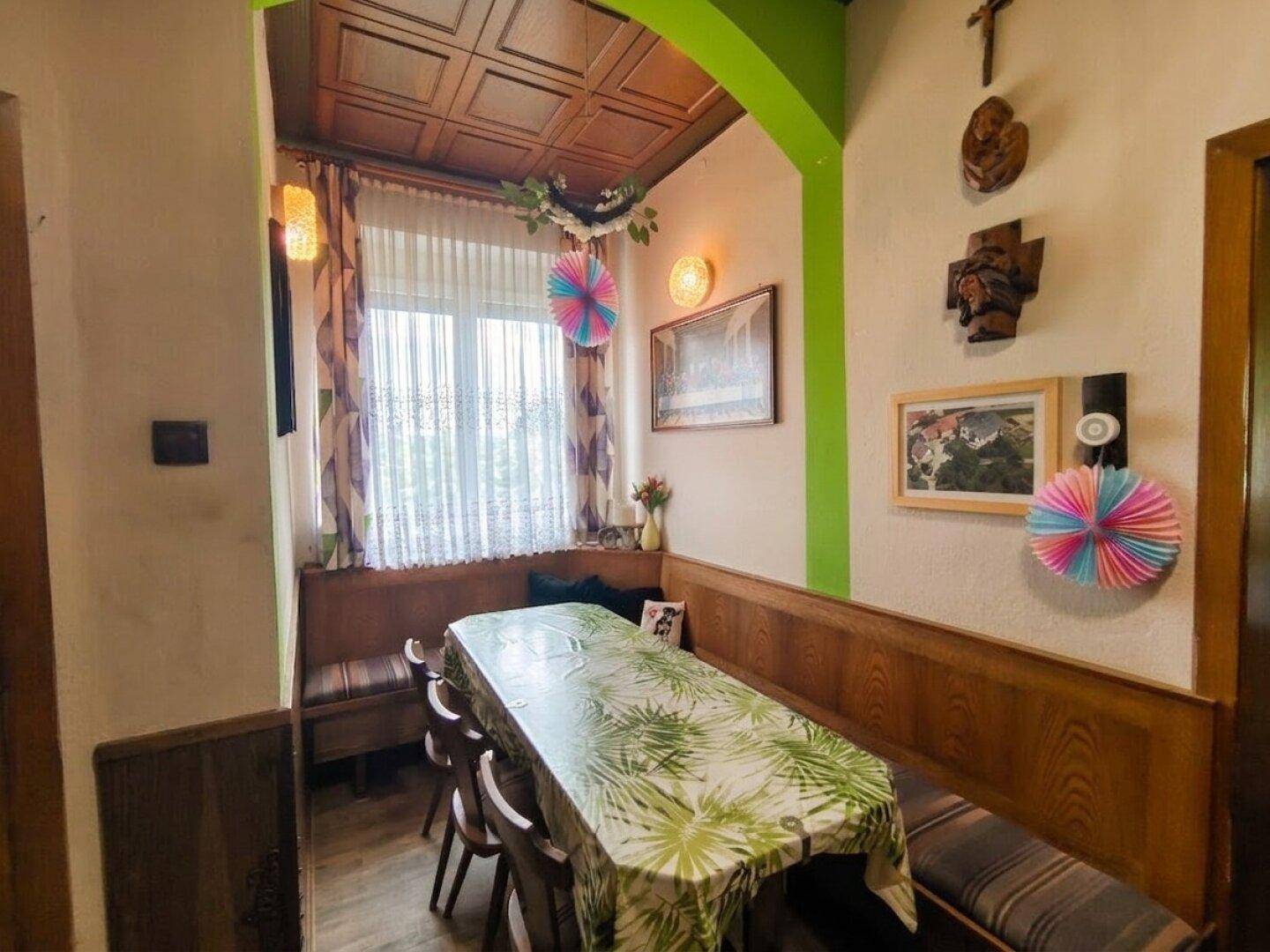 Gemütlicher Essbereich mit langem Tisch, eingebauten Holzbänken und traditioneller Dekoration am Fenster.