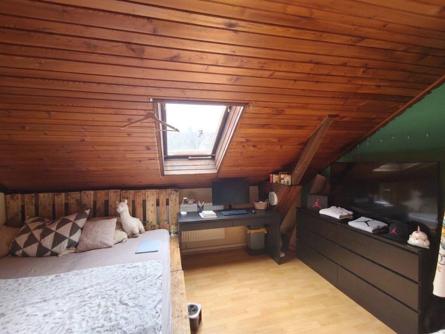Dachschlafzimmer mit schräger Holzdecke, Bett und einem Dachfenster für natürliches Licht.