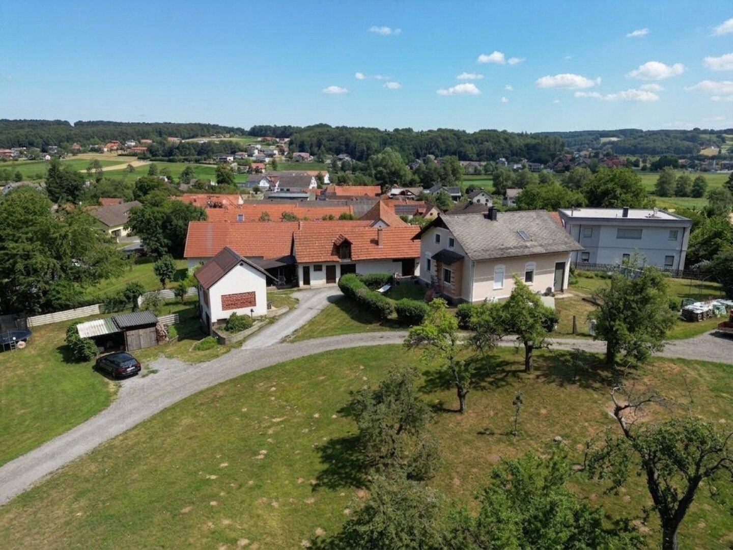 Weitläufige Luftaufnahme eines ländlichen Anwesens mit mehreren Gebäuden und umliegender Natur unter blauem Himmel.