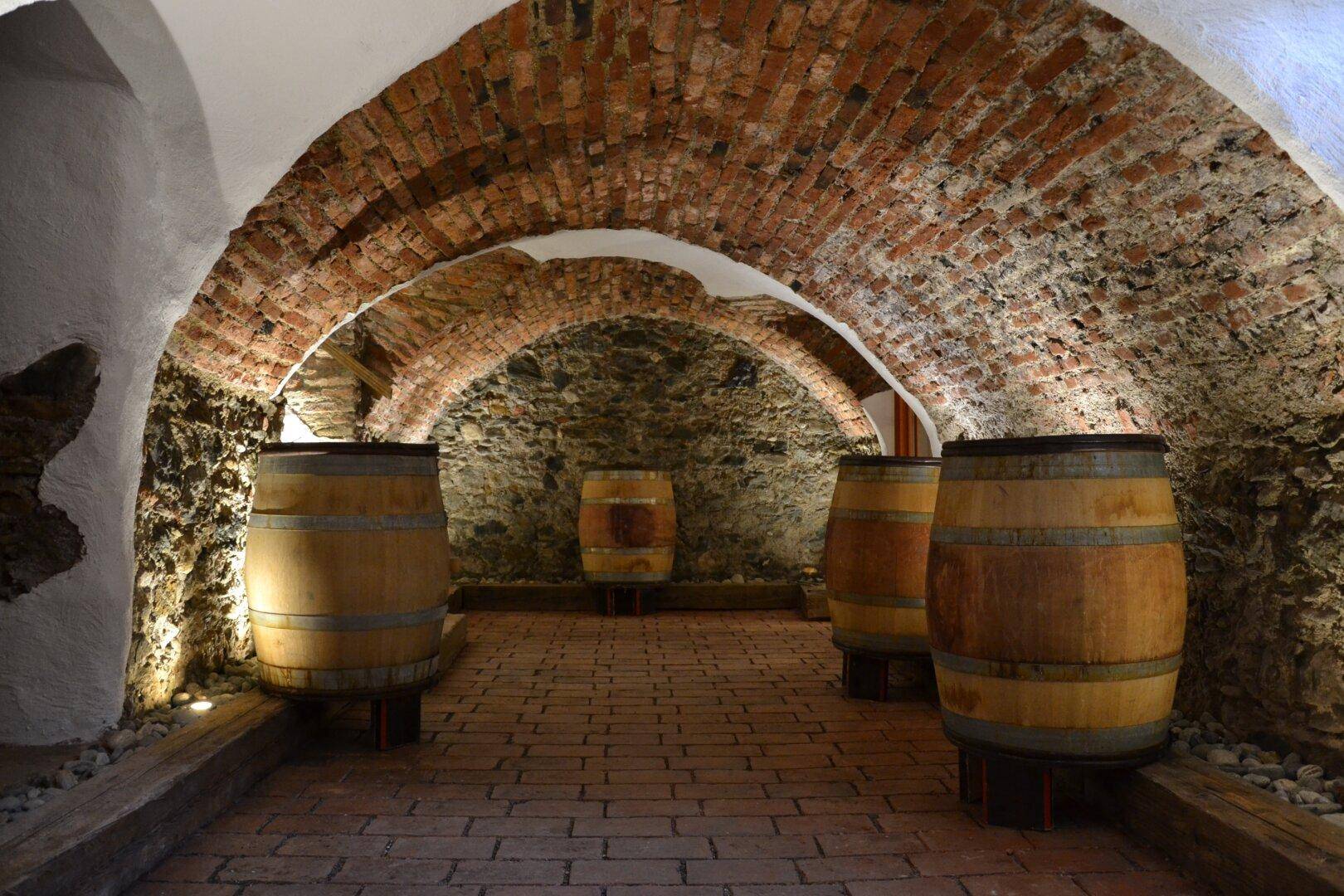 Historischer Weinkeller mit Ziegelgewölbe, Steinmauern und mehreren Holzfässern.
