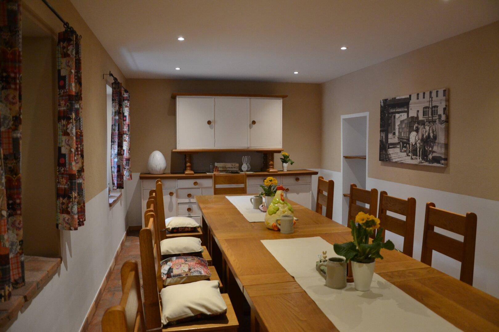 Langer Esstisch aus Holz mit passenden Stühlen und einem weißen Sideboard im Hintergrund.
