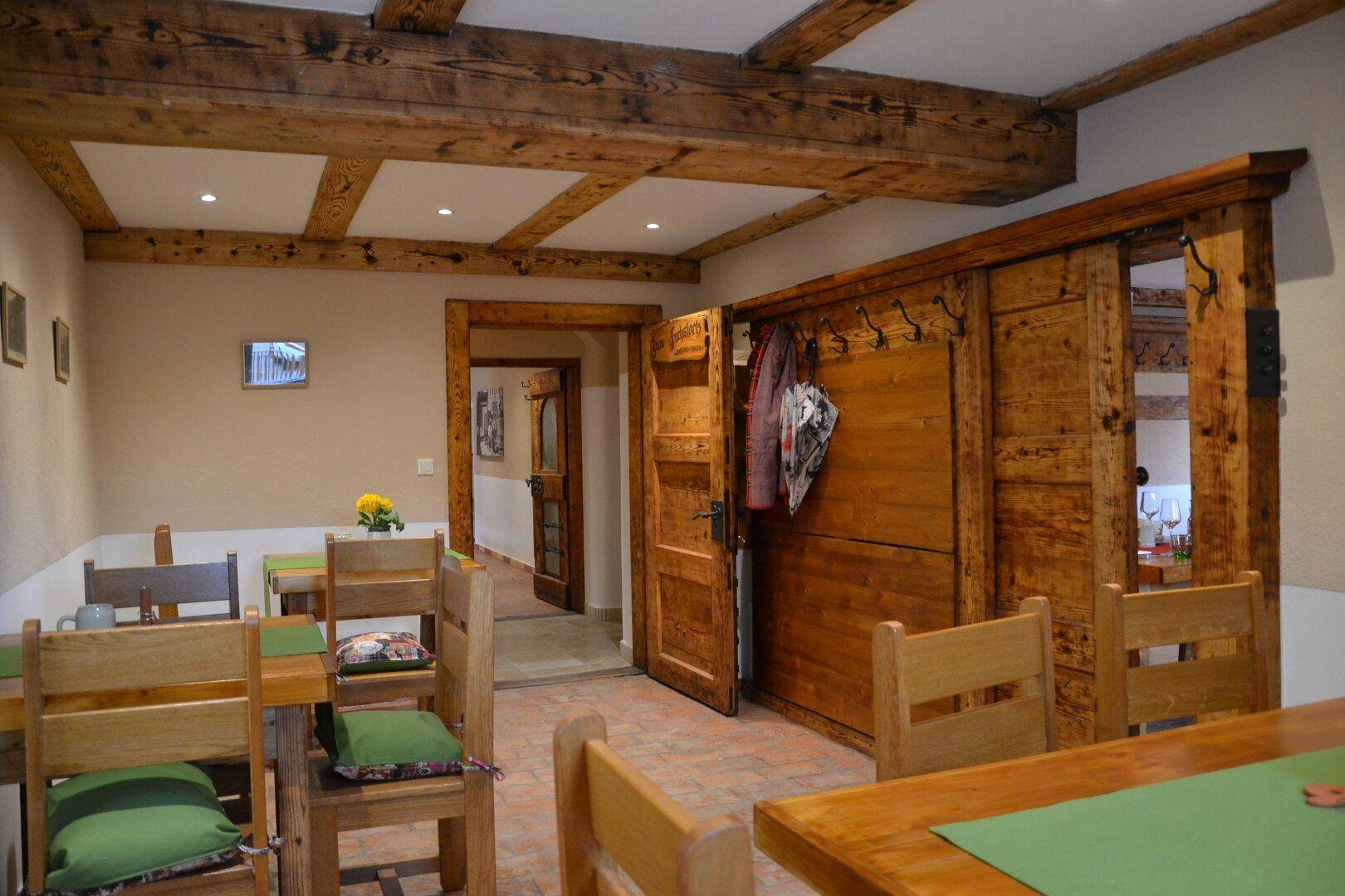 Speisesaal mit Holztischen, sichtbaren Deckenbalken und einer rustikalen Holzwandgarderobe.