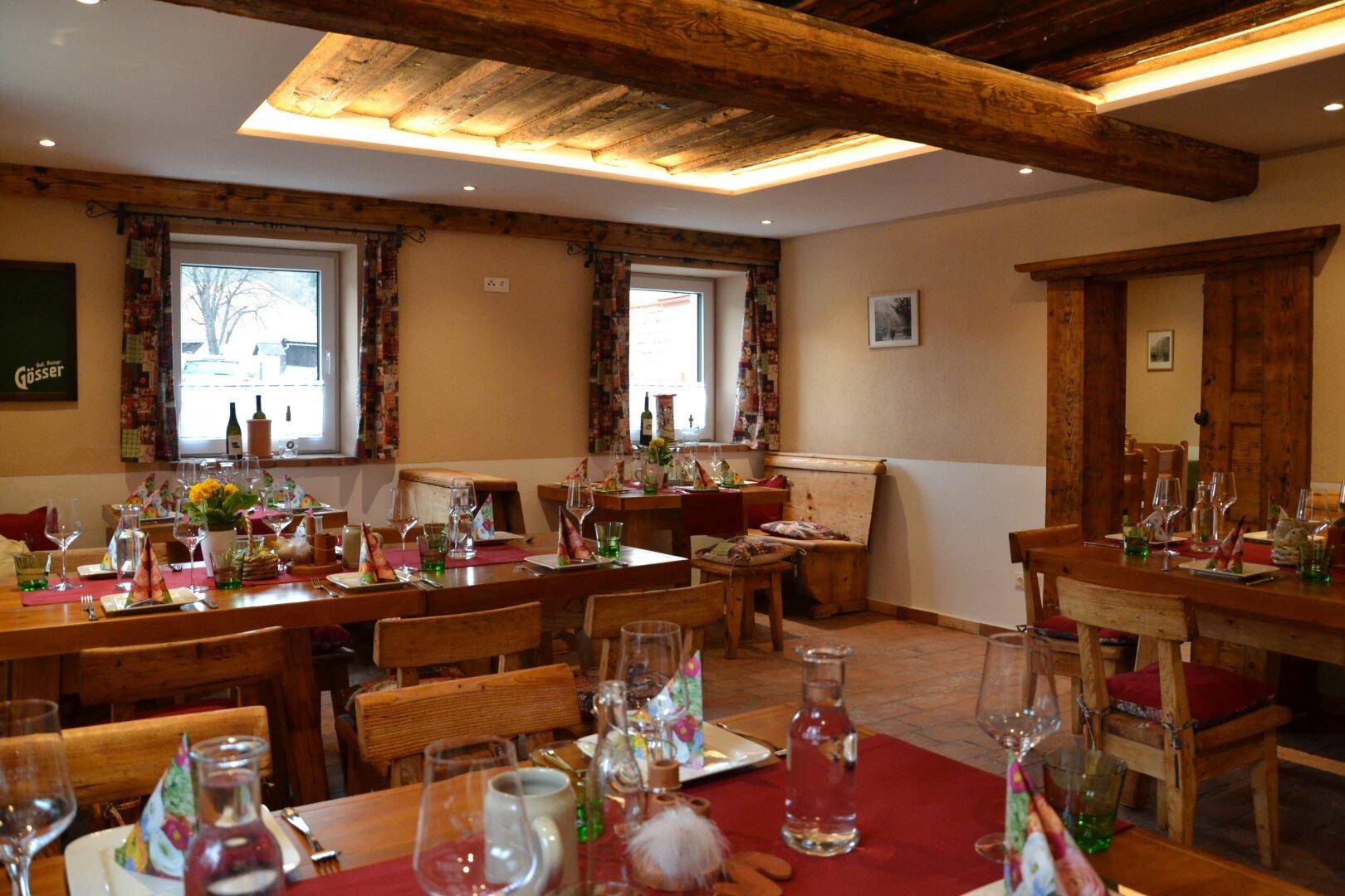 Rustikaler Speisesaal mit Holztischen, roten Tischläufern und sichtbaren Deckenbalken.