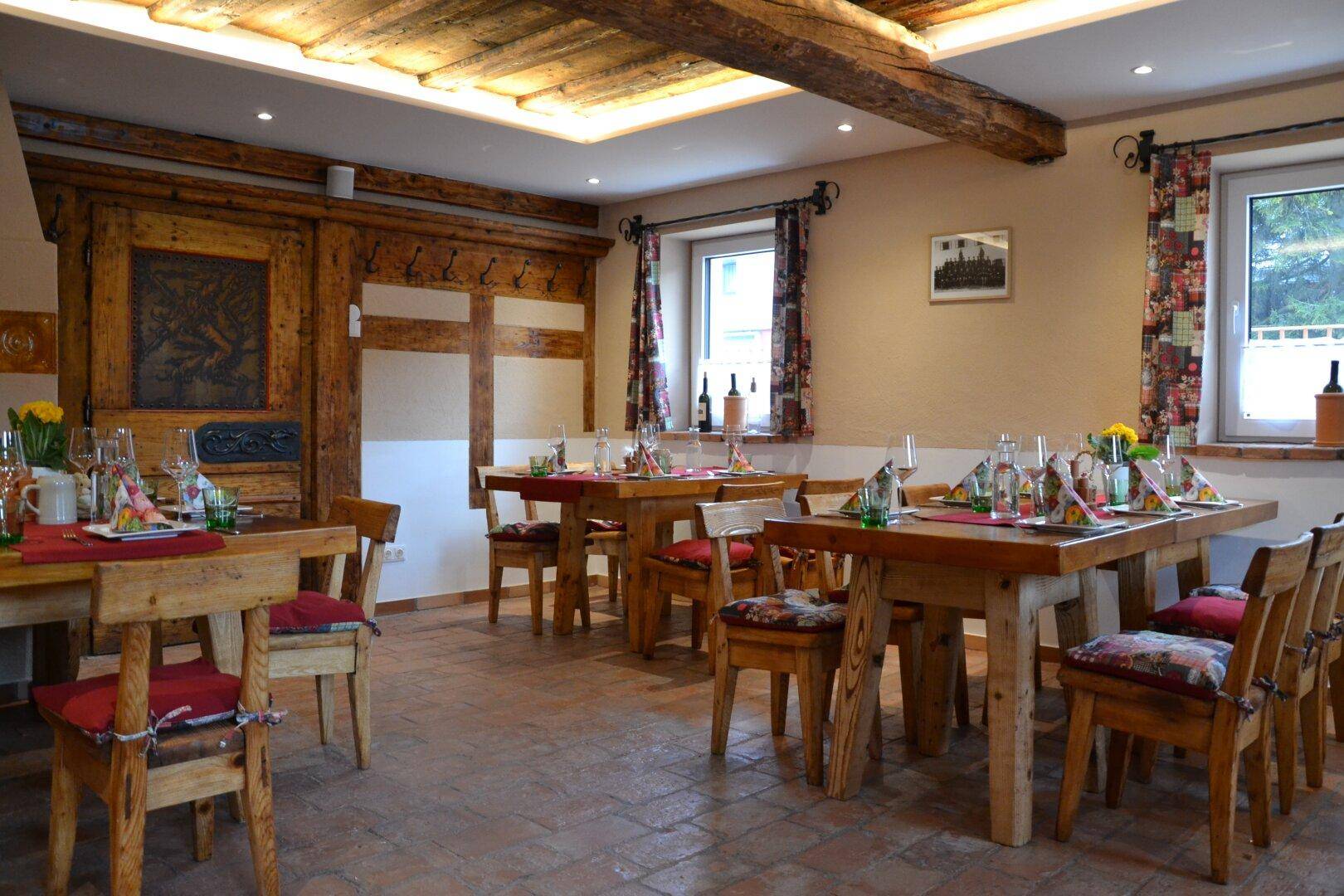 Gemütlicher Speisesaal mit Holztischen, gepolsterten Stühlen und traditionellen Holzelementen.