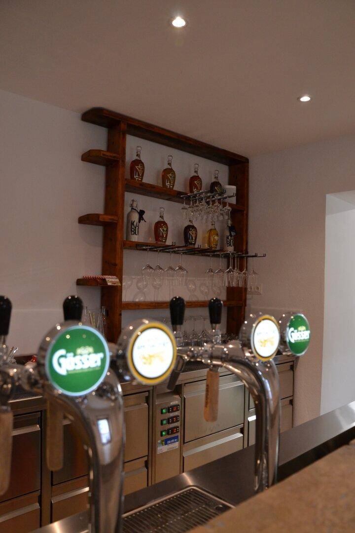 Nahaufnahme von Zapfhähnen und einer Holzregalwand mit Gläsern und Flaschen.
