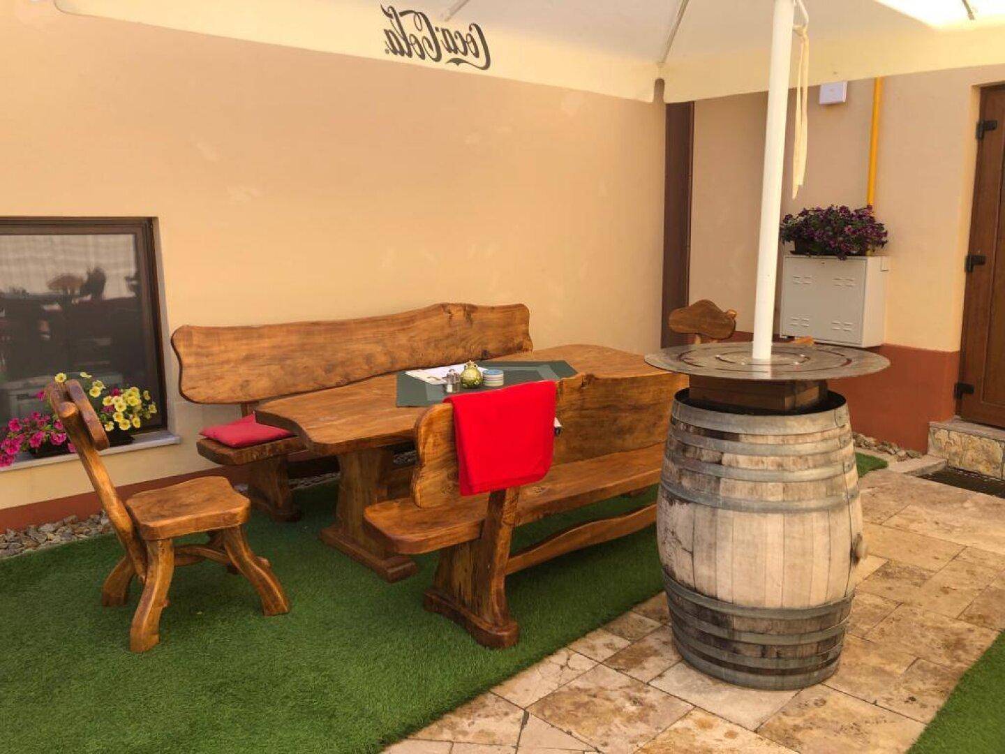 Rustikale Sitzgruppe aus Holz auf einer Außenterrasse mit Kunstrasen und Sonnenschirm.
