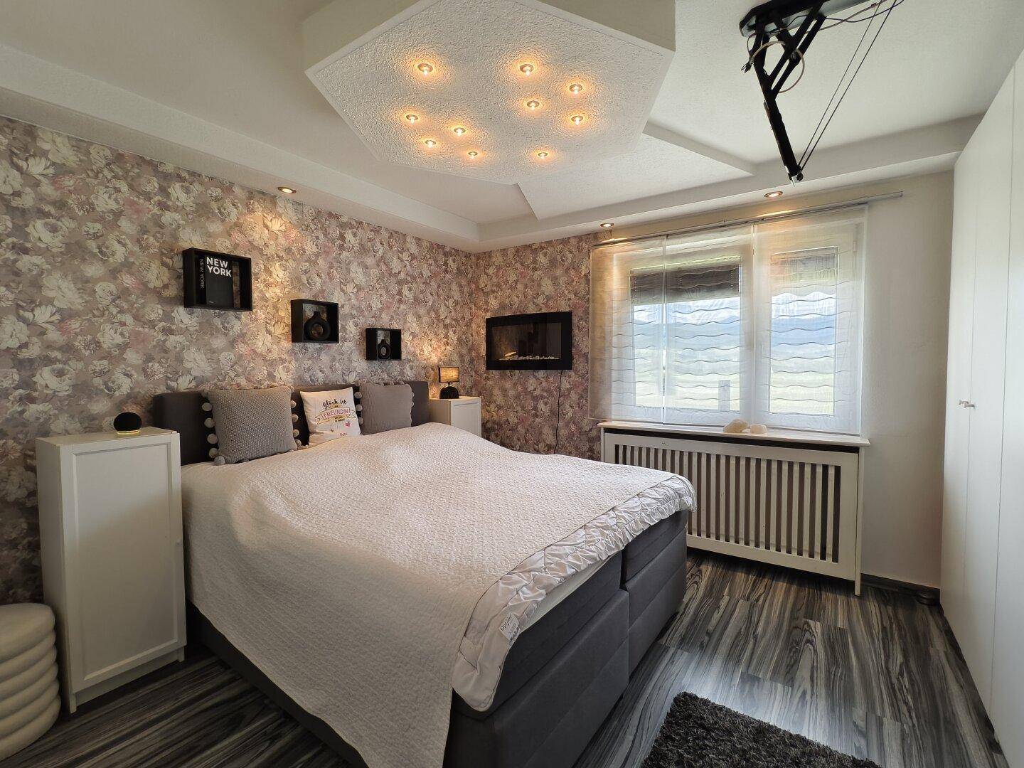 Gemütliches Schlafzimmer mit großem Bett, gemusterter Tapete und Fenster.