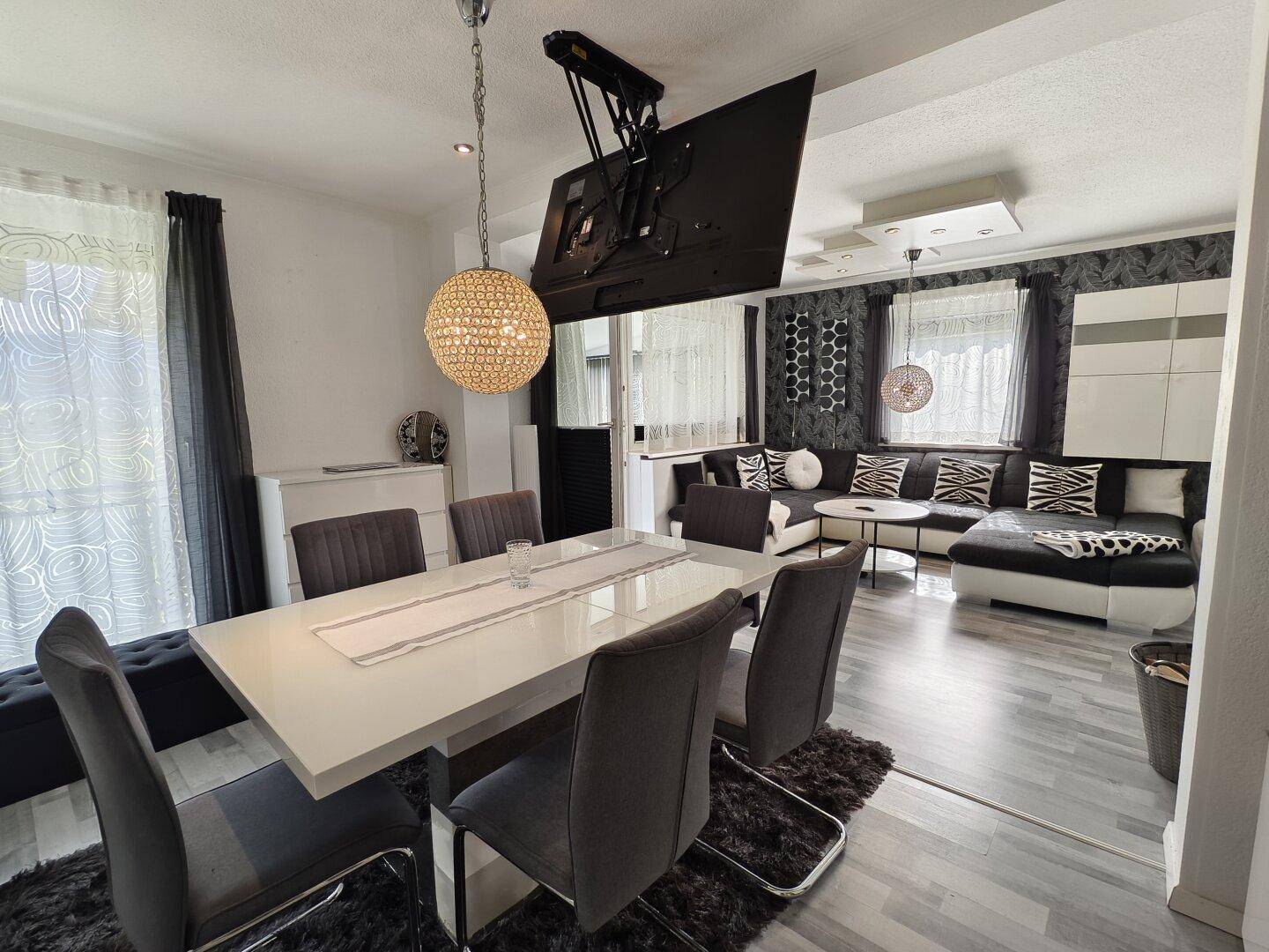 Eleganter Essbereich mit großem Tisch, modernen Stühlen und einem versenkbaren Fernseher an der Decke.