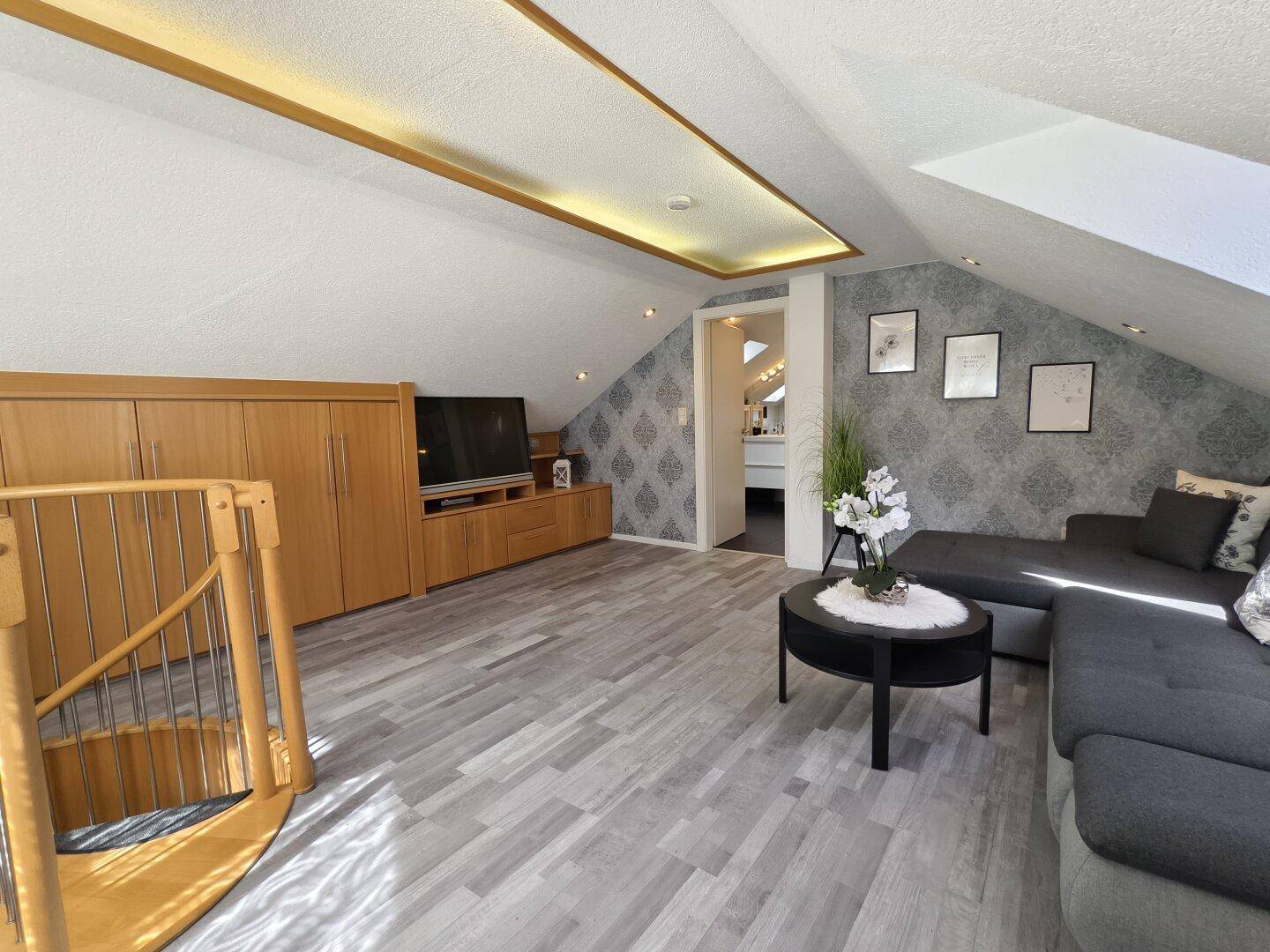 Geräumiger Wohnbereich im Dachgeschoss mit Schrägen, Sofa und Wendeltreppe.