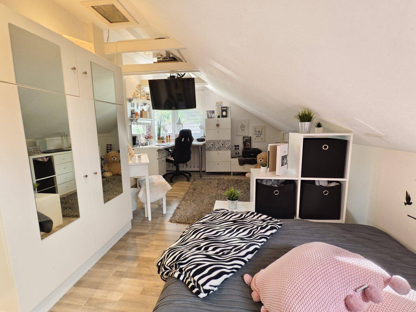 Helles Schlafzimmer im Dachgeschoss mit Schrägen, Bett und Spiegelschränken.