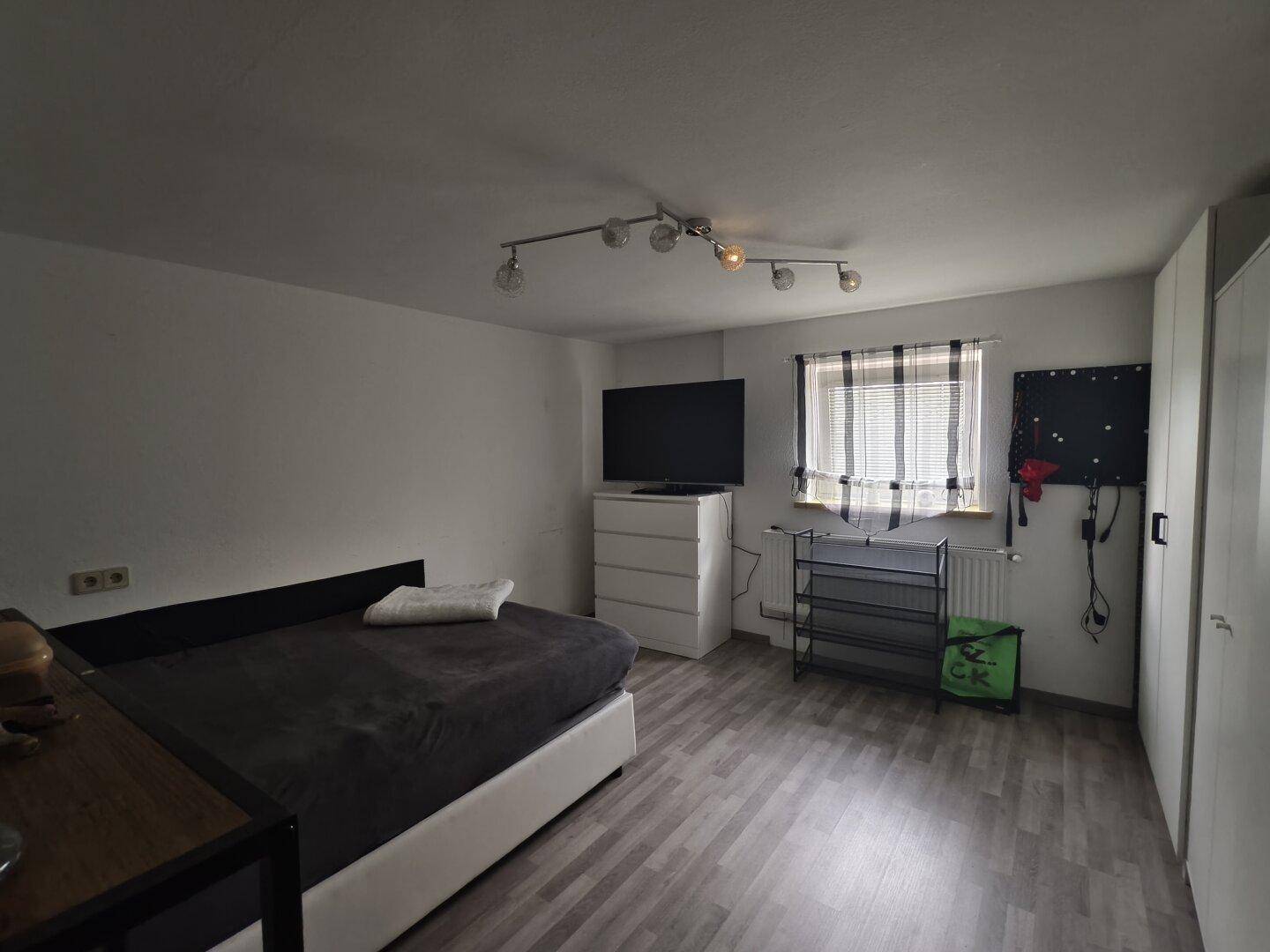 Einfaches Schlafzimmer mit Bett, Kommode und Fenster.