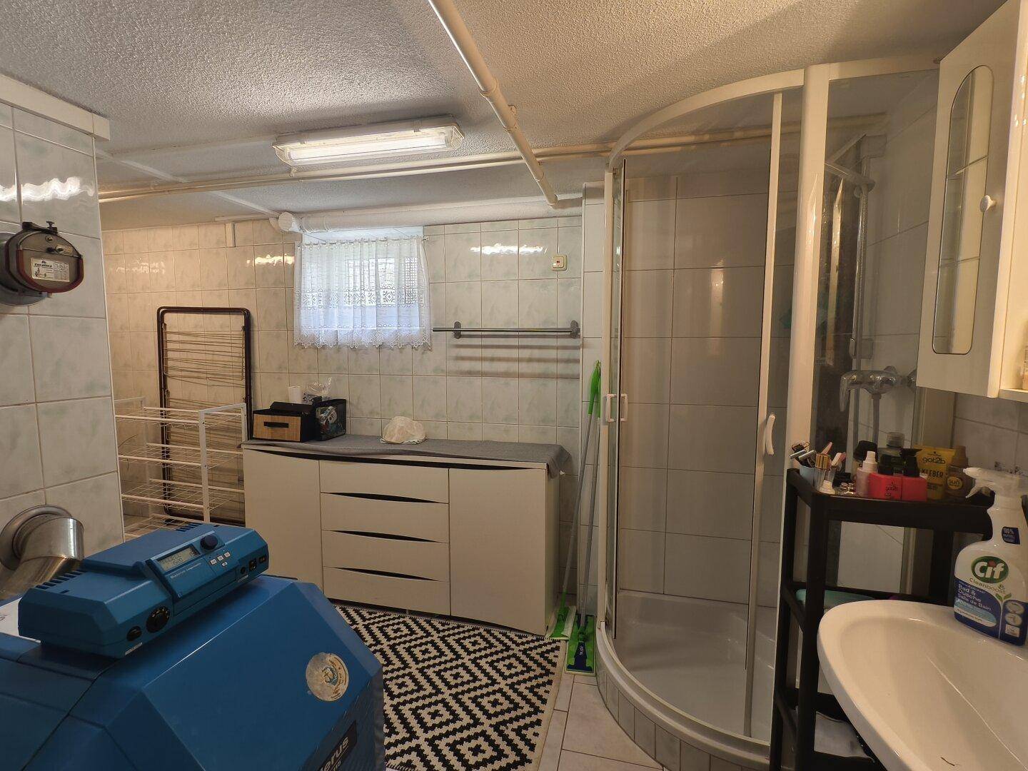 Praktischer Hauswirtschaftsraum im Keller mit Dusche, Waschbecken und Wäscheständer.
