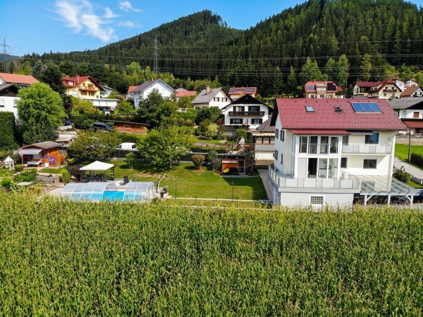 Weitläufige Ansicht eines Wohnhauses mit großem Garten, Pool und angrenzenden Feldern vor einer Bergkulisse.