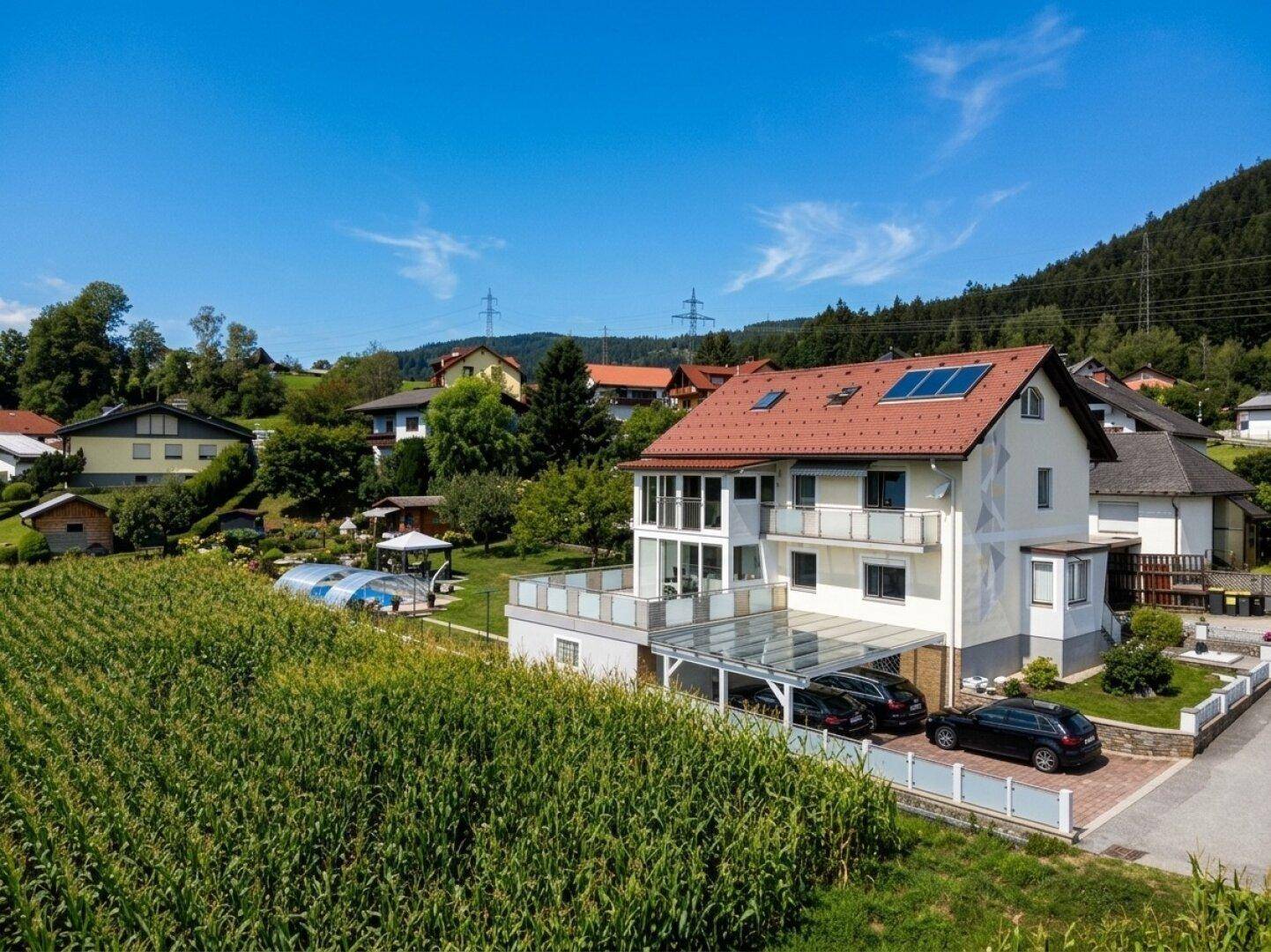 Ansicht des modernen Wohnhauses mit Carport und Poolbereich, eingebettet in eine ländliche Umgebung mit Feldern.