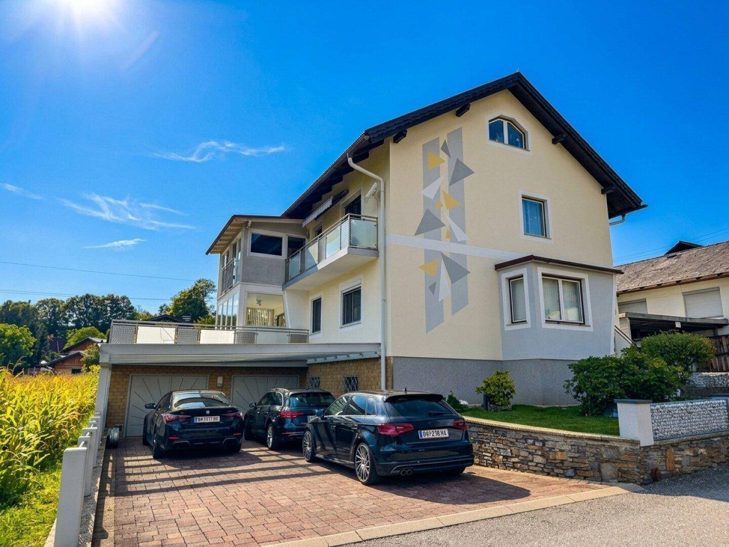 Vorderansicht des Hauses mit Garage, gepflasterter Auffahrt und moderner Fassadengestaltung unter blauem Himmel.