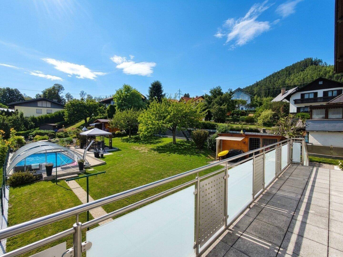 Blick vom Balkon auf den weitläufigen Garten mit Pool, Pavillon und die grüne Hügellandschaft.