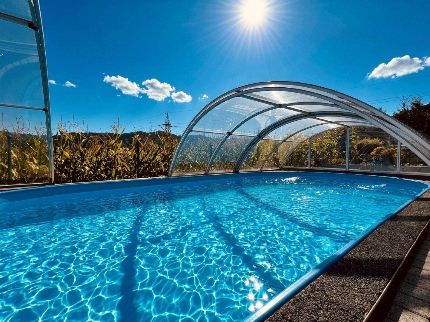 Großzügiger Swimmingpool mit transparenter Überdachung unter strahlend blauem Himmel.