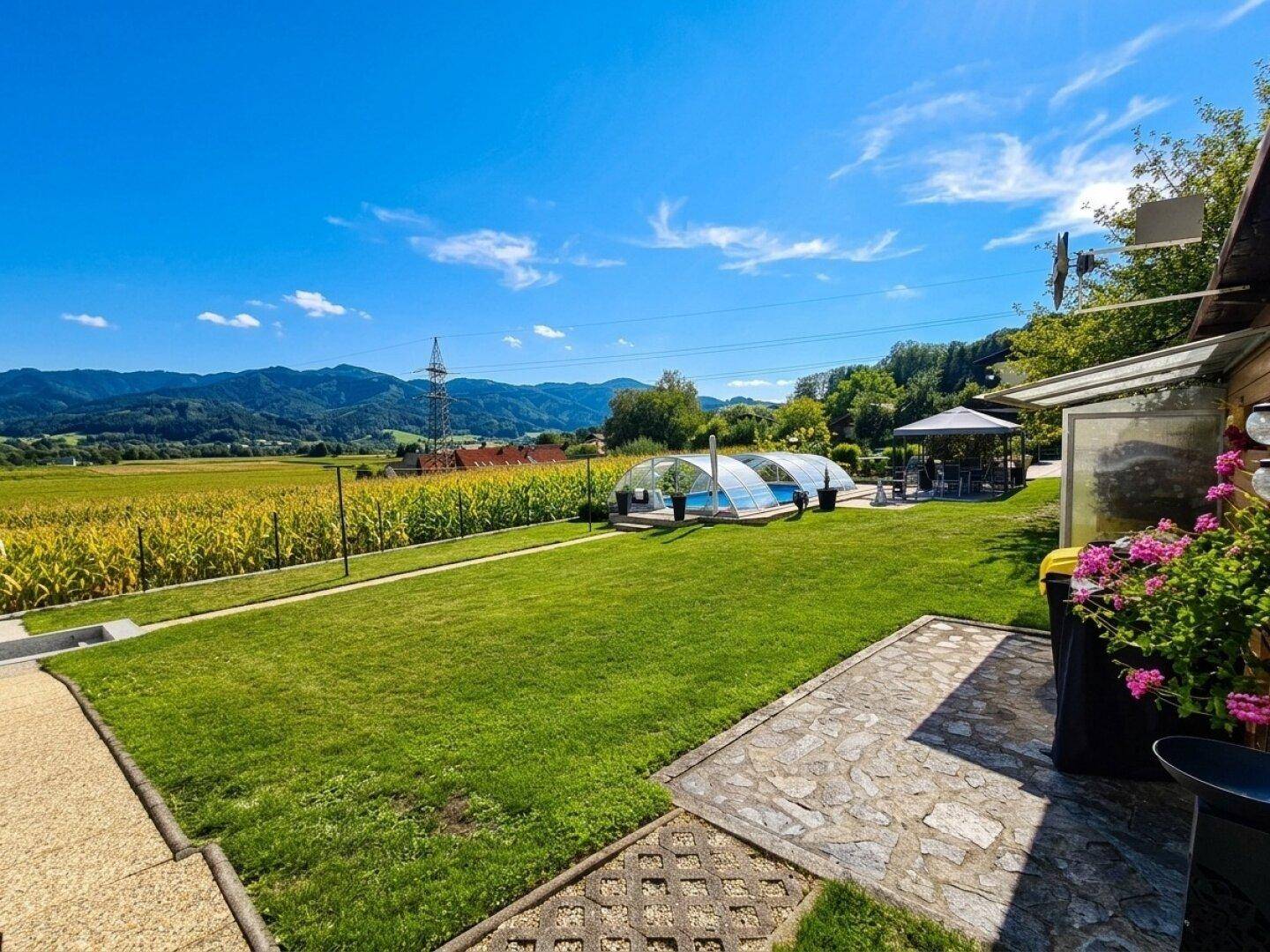 Große Rasenfläche mit Blick auf den Pool, Pavillon und die weite Landschaft mit Feldern und Bergen.